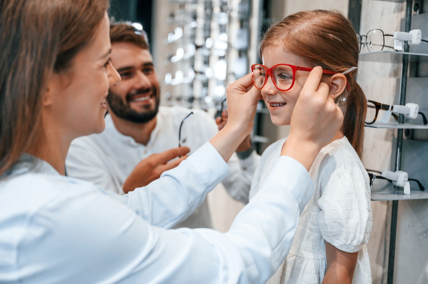 Optometric assistant trying some glasses on a little girl